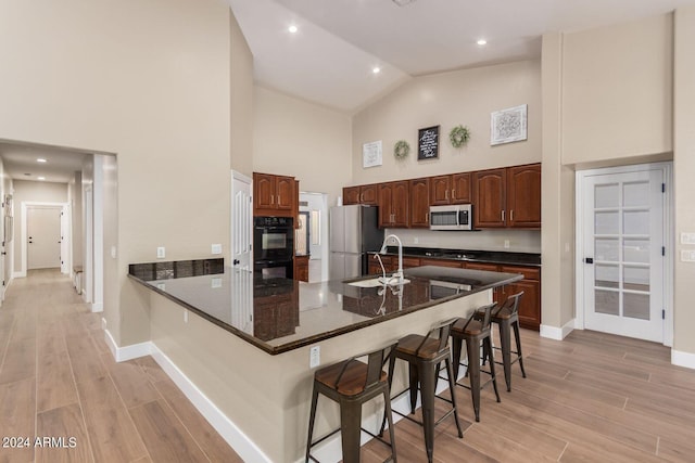 kitchen with sink, a breakfast bar, stainless steel appliances, high vaulted ceiling, and light hardwood / wood-style floors