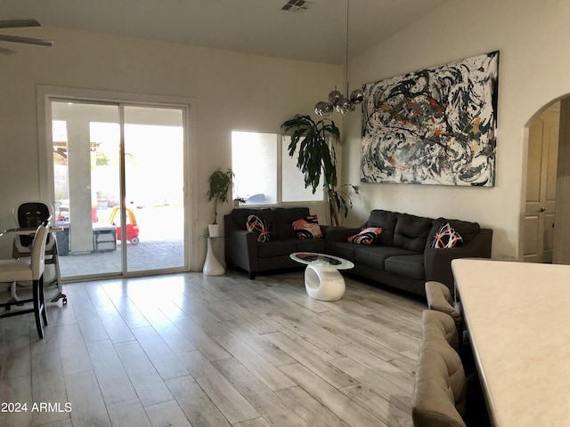 living room with ceiling fan with notable chandelier, light wood-type flooring, and lofted ceiling