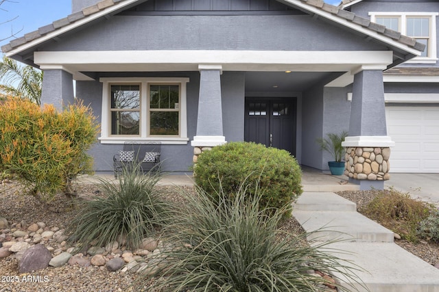 doorway to property featuring a garage, covered porch, a tiled roof, and stucco siding