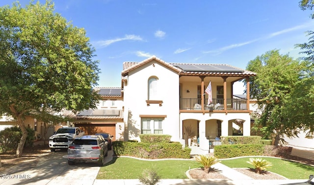 mediterranean / spanish-style house featuring stucco siding, solar panels, driveway, and a balcony