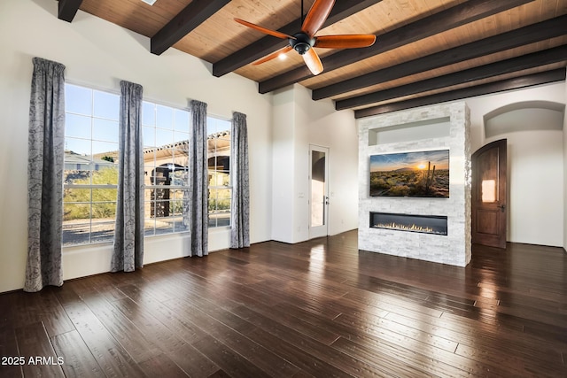 unfurnished living room featuring dark wood-type flooring, ceiling fan, beam ceiling, a fireplace, and wooden ceiling