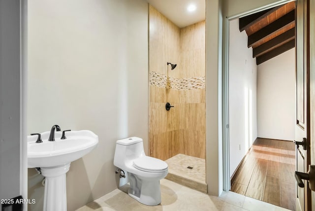 bathroom featuring tiled shower, sink, beam ceiling, and toilet