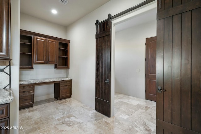 kitchen featuring light stone countertops, a barn door, dark brown cabinets, and built in desk