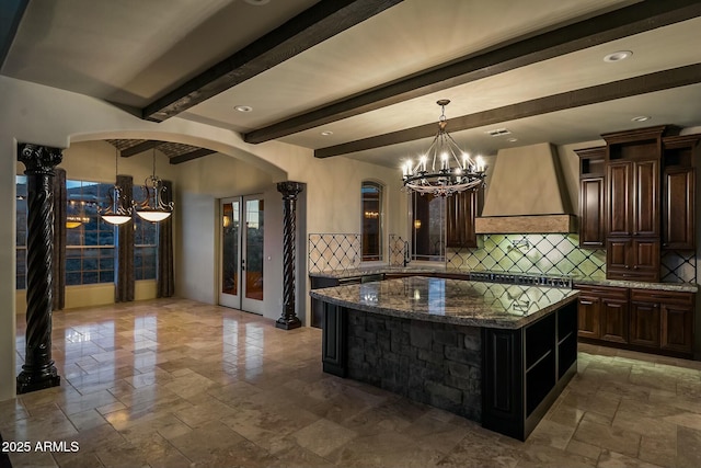 kitchen featuring dark brown cabinetry, custom exhaust hood, a chandelier, a center island, and dark stone countertops