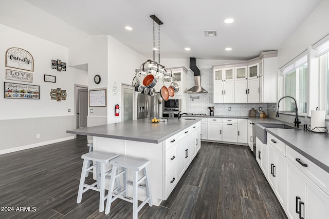 kitchen featuring a center island, dark hardwood / wood-style floors, white cabinets, wall chimney range hood, and decorative light fixtures