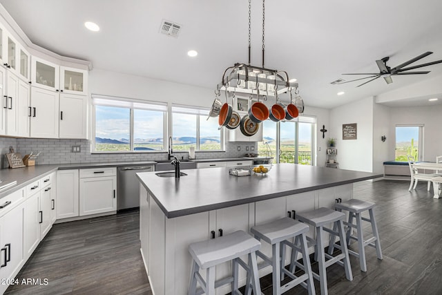 kitchen featuring decorative backsplash, white cabinetry, dark wood-type flooring, dishwasher, and a center island with sink