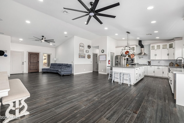 kitchen featuring stainless steel fridge, a kitchen island, wall chimney exhaust hood, dark hardwood / wood-style floors, and a breakfast bar area