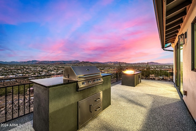 patio terrace at dusk with a mountain view, a grill, and exterior kitchen