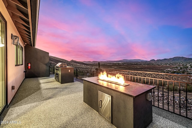 patio terrace at dusk featuring a mountain view, area for grilling, and a fire pit