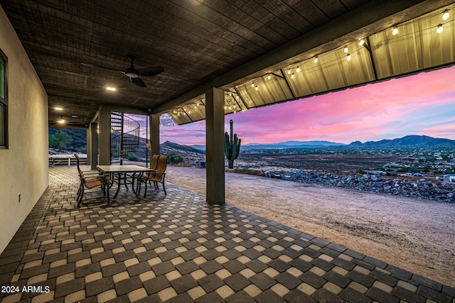 patio terrace at dusk featuring ceiling fan and a mountain view