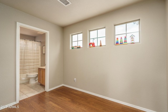 unfurnished bedroom with visible vents, baseboards, ensuite bathroom, and light wood finished floors