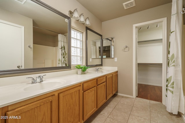 bathroom with visible vents, double vanity, a sink, a spacious closet, and tile patterned floors