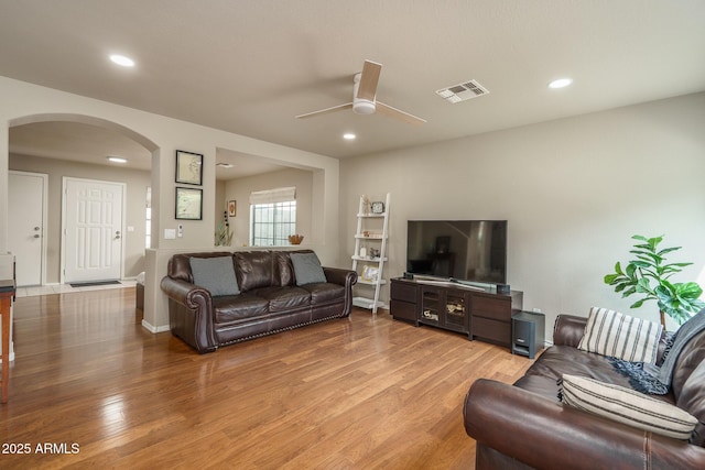 living room featuring a ceiling fan, visible vents, recessed lighting, arched walkways, and light wood-style floors