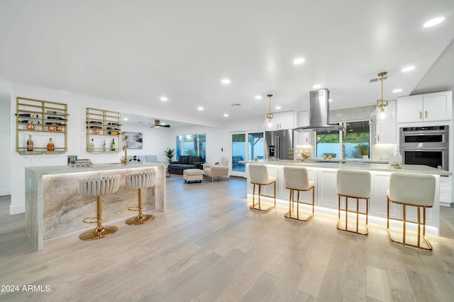 kitchen featuring white cabinets, island range hood, hanging light fixtures, and appliances with stainless steel finishes