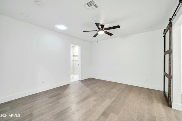 spare room with a barn door, ceiling fan, and light hardwood / wood-style flooring