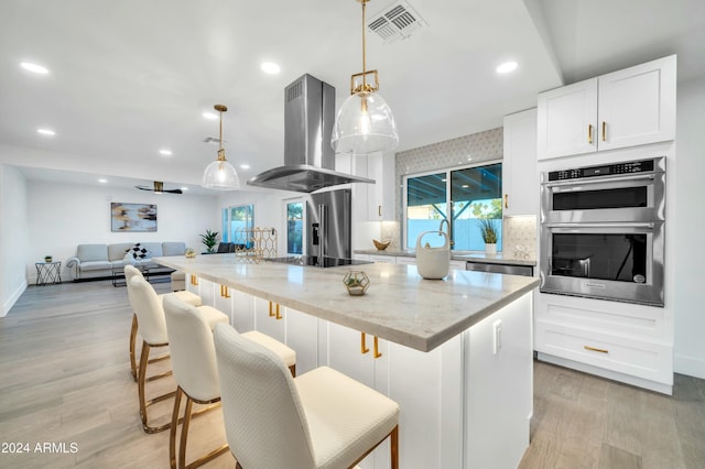 kitchen featuring light stone counters, island range hood, double oven, a spacious island, and white cabinets