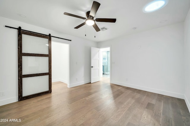 empty room featuring a barn door, ceiling fan, and light hardwood / wood-style flooring