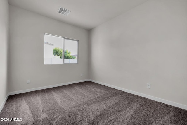 unfurnished room with baseboards, visible vents, and dark carpet