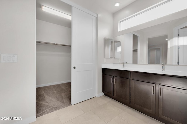 full bath with double vanity, baseboards, tile patterned flooring, a walk in closet, and a sink