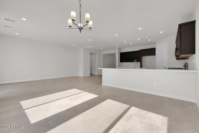 unfurnished living room with a notable chandelier, baseboards, a sink, and recessed lighting