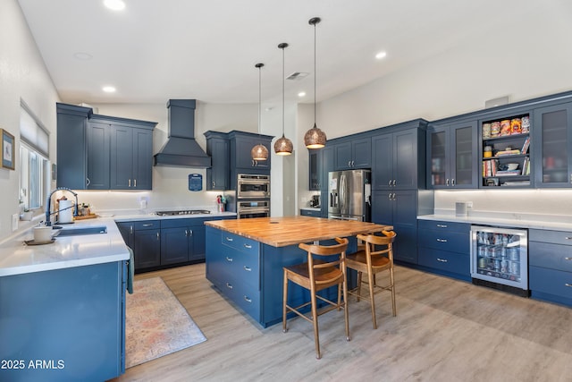 kitchen with appliances with stainless steel finishes, premium range hood, beverage cooler, sink, and a kitchen island