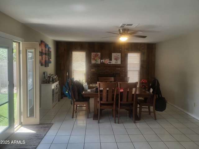 dining space with visible vents, a ceiling fan, light tile patterned flooring, and wooden walls