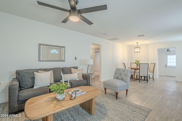 living room with ceiling fan with notable chandelier and light hardwood / wood-style flooring