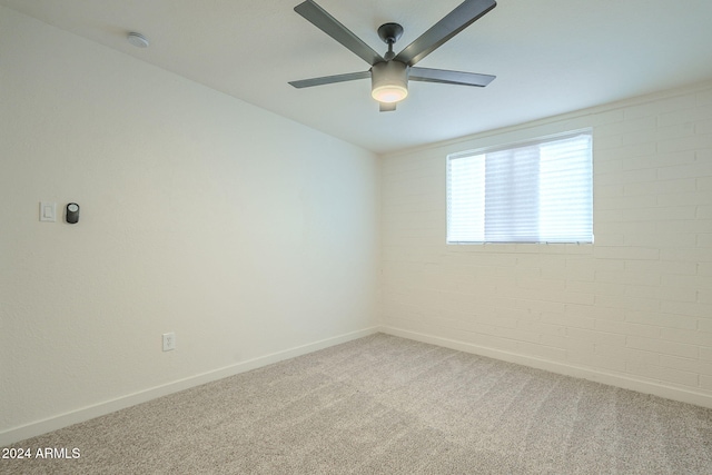 carpeted empty room featuring ceiling fan and brick wall