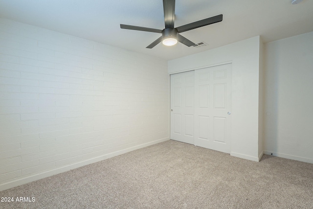 unfurnished bedroom with ceiling fan, a closet, light carpet, and brick wall