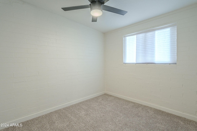 unfurnished room featuring carpet flooring, ceiling fan, and brick wall