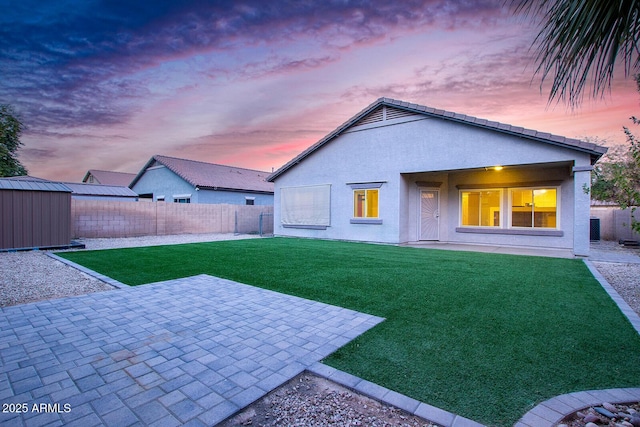 back house at dusk featuring a yard, a patio, and a storage shed