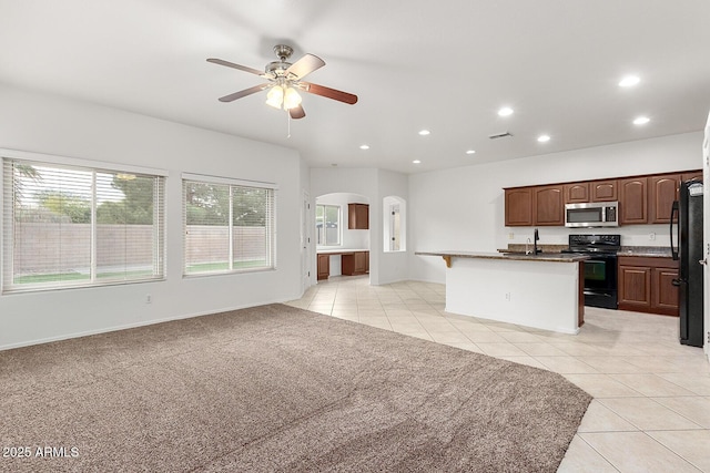 kitchen with a breakfast bar, black appliances, ceiling fan, light tile patterned floors, and an island with sink