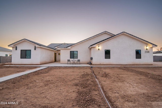 back of house at dusk with a patio area, fence, and stucco siding