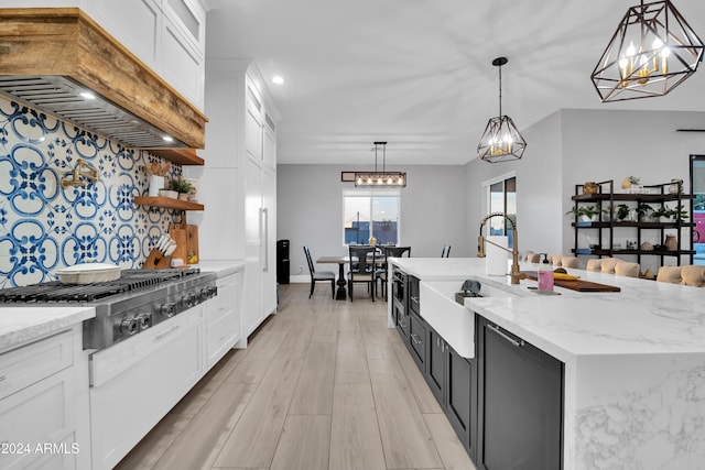 kitchen featuring stainless steel gas cooktop, a kitchen island with sink, white cabinetry, and pendant lighting