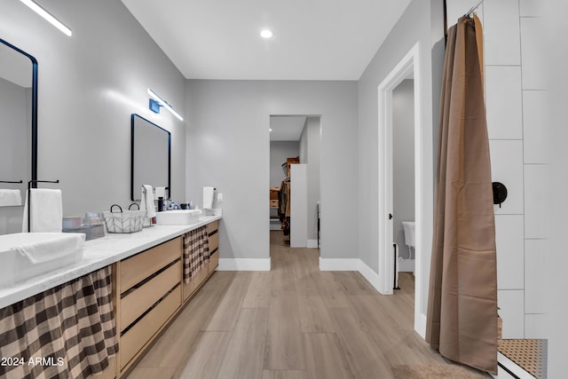 bathroom featuring double vanity, baseboards, toilet, wood finished floors, and a sink