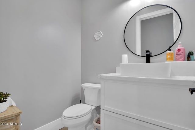 half bathroom with vanity, toilet, and baseboards