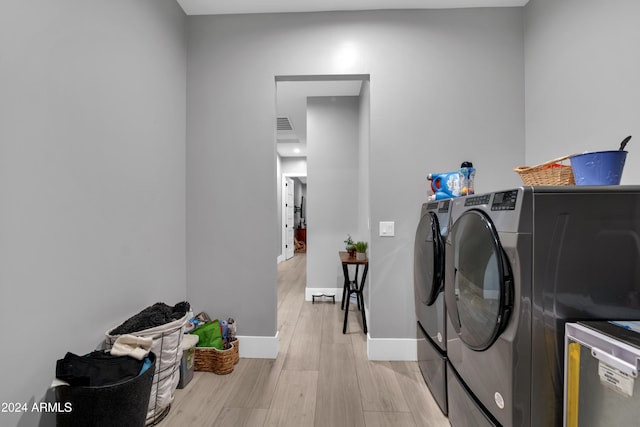 clothes washing area with laundry area, washing machine and clothes dryer, light wood-style flooring, and baseboards