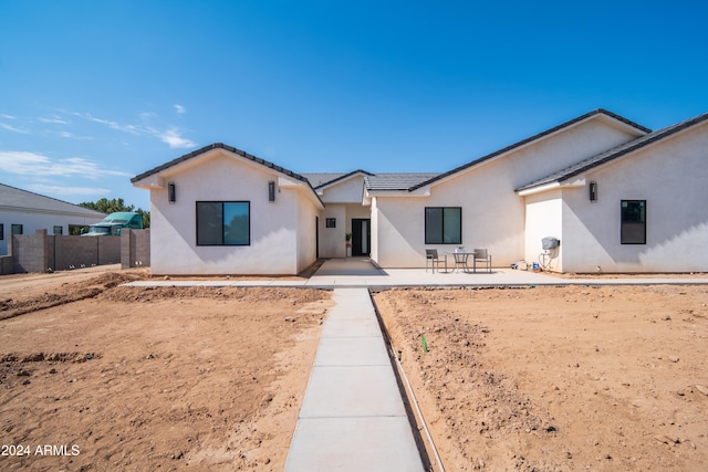 view of front facade featuring a patio, a tile roof, fence, and stucco siding