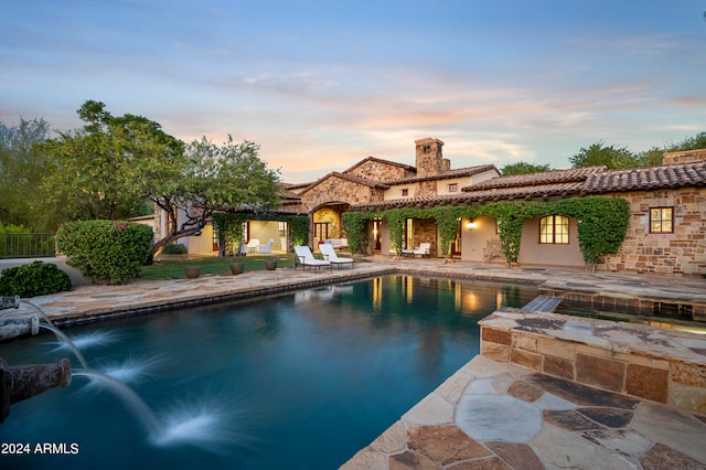 pool at dusk with pool water feature and a patio area