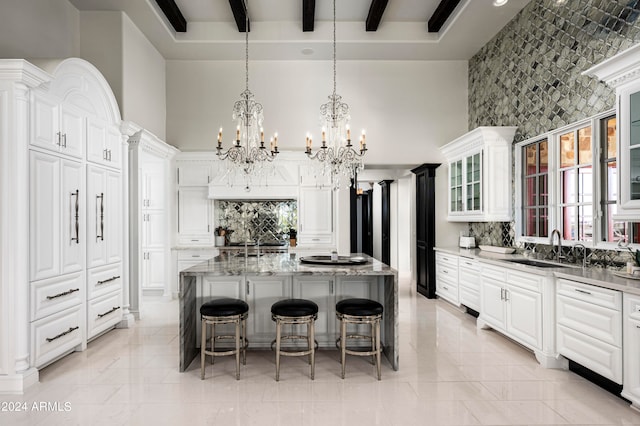 kitchen featuring sink, light stone counters, a center island with sink, and beam ceiling