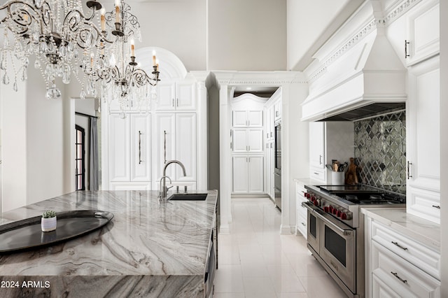 kitchen with an inviting chandelier, custom range hood, sink, pendant lighting, and double oven range