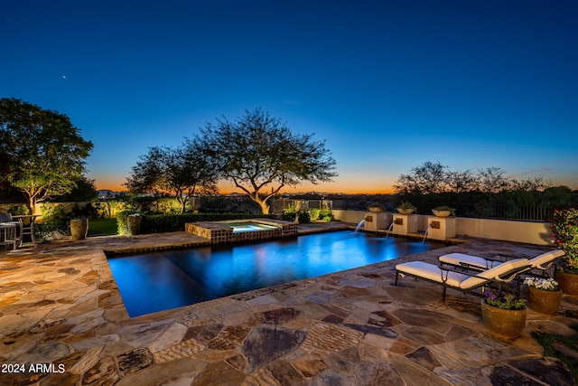 pool at dusk with an in ground hot tub, pool water feature, and a patio