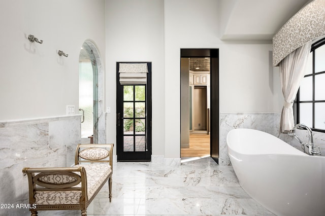 bathroom featuring tile walls, a high ceiling, and a bathtub