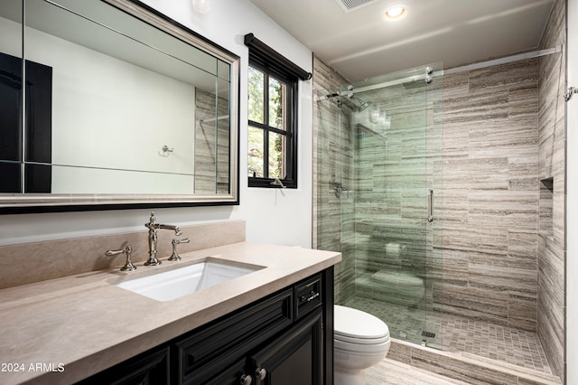 bathroom featuring a shower with door, vanity, and toilet