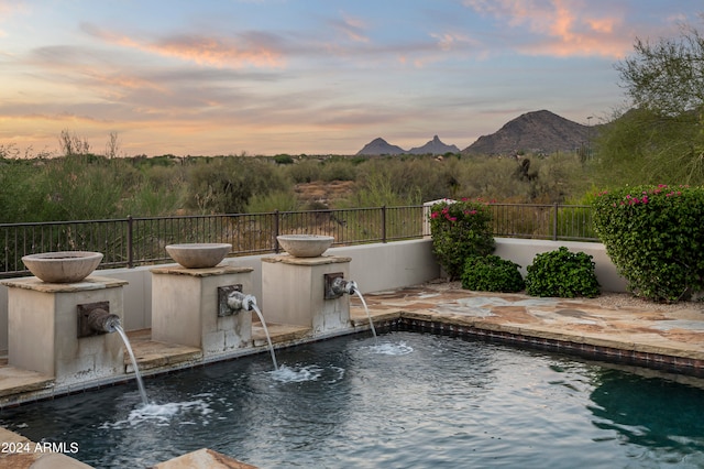 pool at dusk with pool water feature and a mountain view