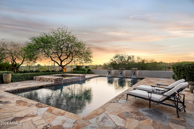 pool at dusk with an in ground hot tub and a patio