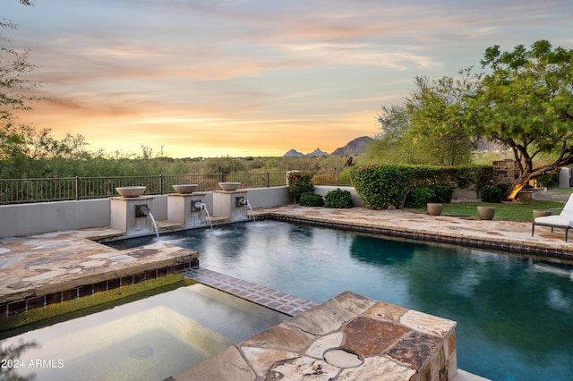 pool at dusk with pool water feature, a patio, and a mountain view