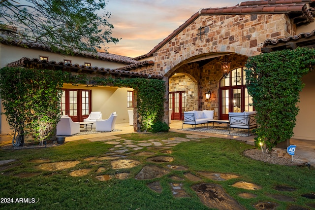 back house at dusk featuring a lawn, a patio area, and french doors