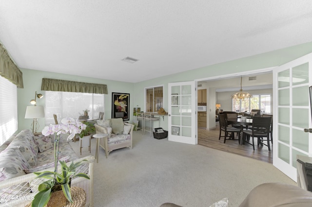 living room featuring an inviting chandelier, french doors, carpet, and a textured ceiling