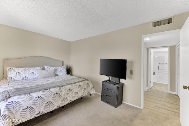 carpeted bedroom with ensuite bathroom and a textured ceiling